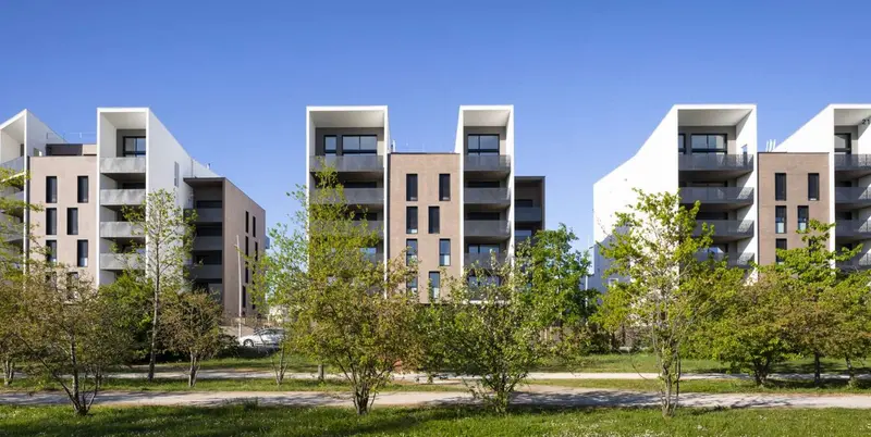 Résidences aux toitures en sheds, derrière un alignement d’arbres
